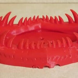May include: A red 3D printed object shaped like a monster's mouth with sharp teeth.