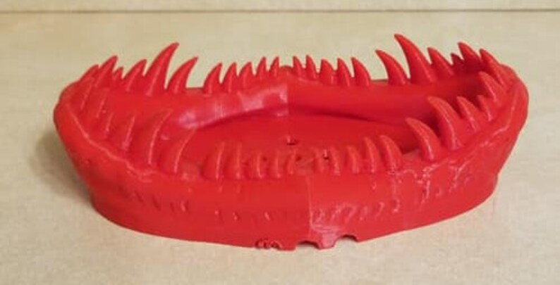 May include: A red 3D printed object shaped like a monster's mouth with sharp teeth.