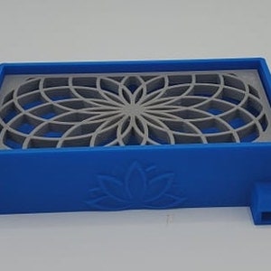 Puede incluir: Un jabonera de pl&aacute;stico azul con un dise&ntilde;o geom&eacute;trico gris y un logotipo de flor de loto. La jabonera tiene un peque&ntilde;o pico en el lateral.
