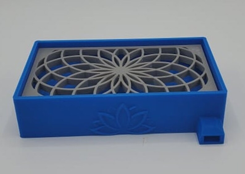 Puede incluir: Un jabonera de pl&aacute;stico azul con un dise&ntilde;o geom&eacute;trico gris y un logotipo de flor de loto. La jabonera tiene un peque&ntilde;o pico en el lateral.