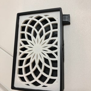 Puede incluir: Una caja impresa en 3D en blanco y negro con un dise&ntilde;o geom&eacute;trico. La caja tiene una peque&ntilde;a pesta&ntilde;a en el lateral.
