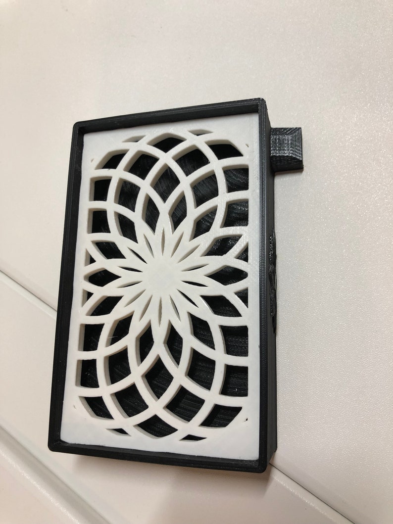 Puede incluir: Una caja impresa en 3D en blanco y negro con un dise&ntilde;o geom&eacute;trico. La caja tiene una peque&ntilde;a pesta&ntilde;a en el lateral.