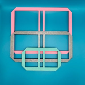 Può includere: Tre forme geometriche nidificate in rosa, argento e verde acqua su sfondo verde acqua. Le forme sono rettangolari con angoli arrotondati e linee interne, che ricordano un design a finestra o cornice. La disposizione è simmetrica.