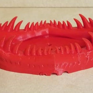 May include: A red 3D printed object shaped like a mouth with sharp teeth. The object is designed to be a decorative dish or tray.