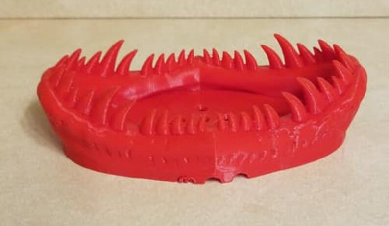 May include: A red 3D printed object shaped like a mouth with sharp teeth. The object is designed to be a decorative dish or tray.