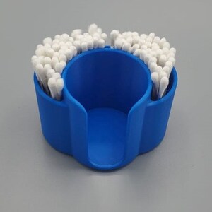 May include: A blue plastic cotton swab holder with a circular opening in the center. The holder is filled with cotton swabs.