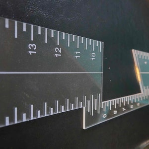 May include: A clear plastic ruler with markings from 6 to 13. The ruler is shaped like a right angle with a shorter side extending from the longer side.