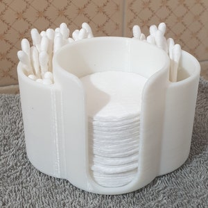 May include: White plastic organizer with three compartments for storing cotton swabs and cotton rounds. The organizer has a rounded shape and is made of a smooth, white plastic.