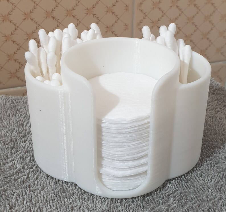 May include: White plastic organizer with three compartments for storing cotton swabs and cotton rounds. The organizer has a rounded shape and is made of a smooth, white plastic.