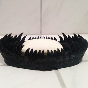 May include: A black soap dish with a spiky, jagged design. A white bar of soap is resting inside the dish.