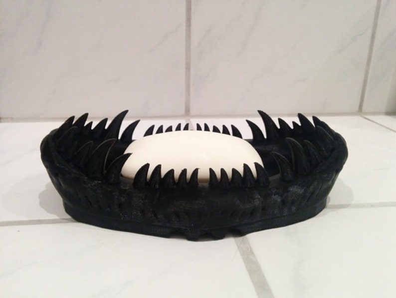 May include: A black soap dish with a spiky, jagged design. A white bar of soap is resting inside the dish.
