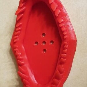 May include: A red plastic soap dish shaped like a mouth with teeth. The dish has five holes in the bottom for drainage.