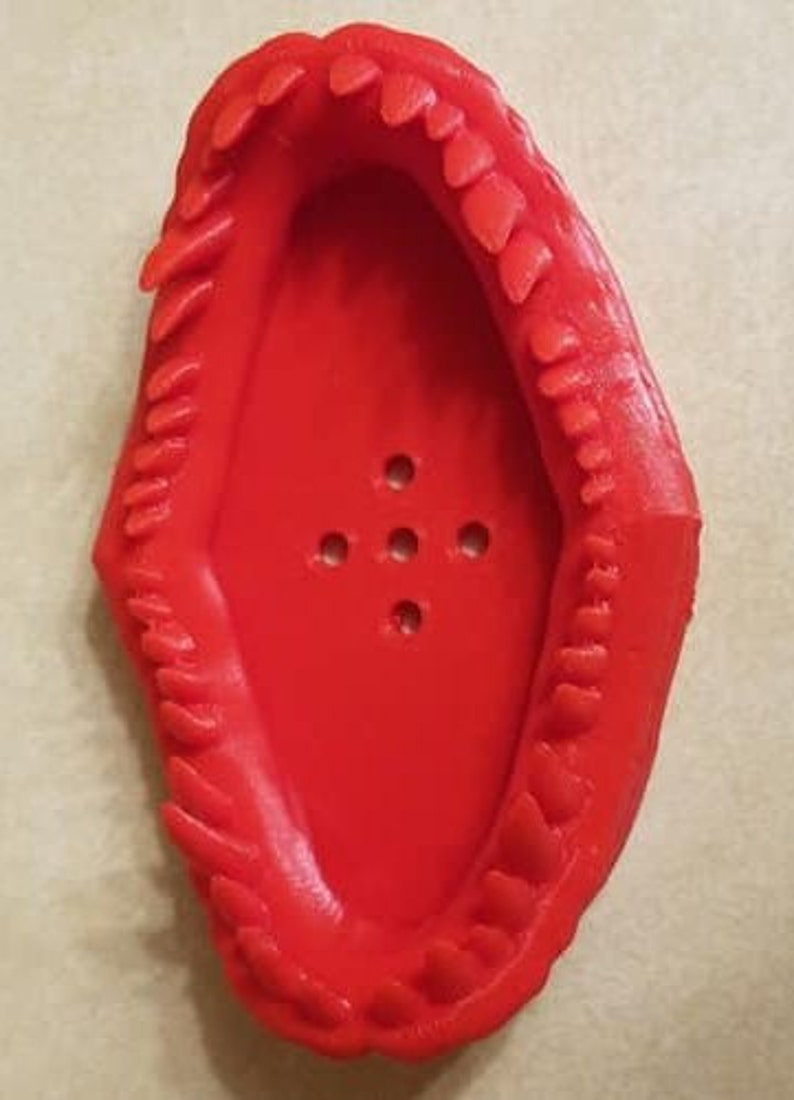 May include: A red plastic soap dish shaped like a mouth with teeth. The dish has five holes in the bottom for drainage.