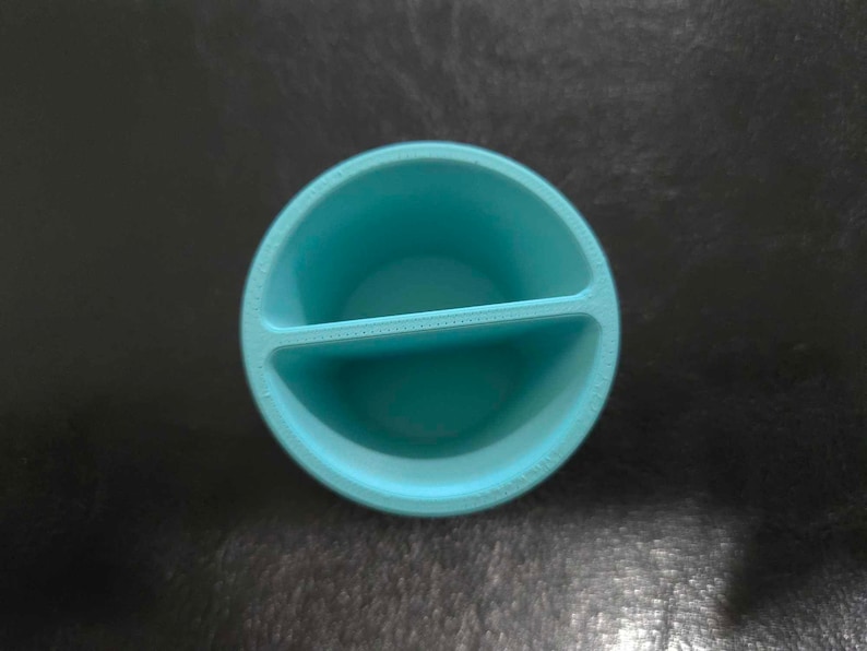 May include: A divided turquoise blue ceramic dish with a rounded shape. The dish has two sections.