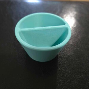 May include: A light blue plastic divided container with two compartments. The container is round and has a smooth surface.