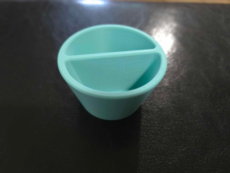 May include: A light blue plastic divided container with two compartments. The container is round and has a smooth surface.