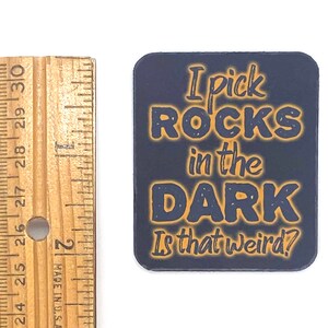 May include: A dark blue square sticker with orange text that reads "I pick ROCKS in the DARK Is that weird?"