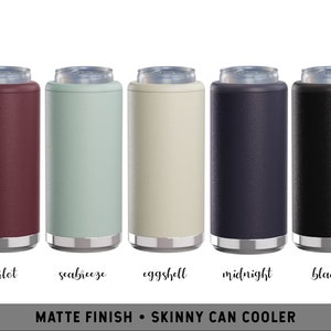 May include: A collection of five matte finish skinny can coolers in various colors: merlot, seabreeze, eggshell, midnight, and black. Each cooler has a silver rim at the top and bottom. The text at the bottom reads "MATTE FINISH &bull; SKINNY CAN COOLER".