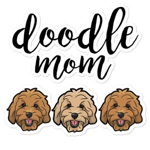 May include: Doodle Mom sticker with three doodle dog faces. The dogs have brown and cream fur, brown noses, and black eyes. The text "doodle mom" is in black cursive lettering.