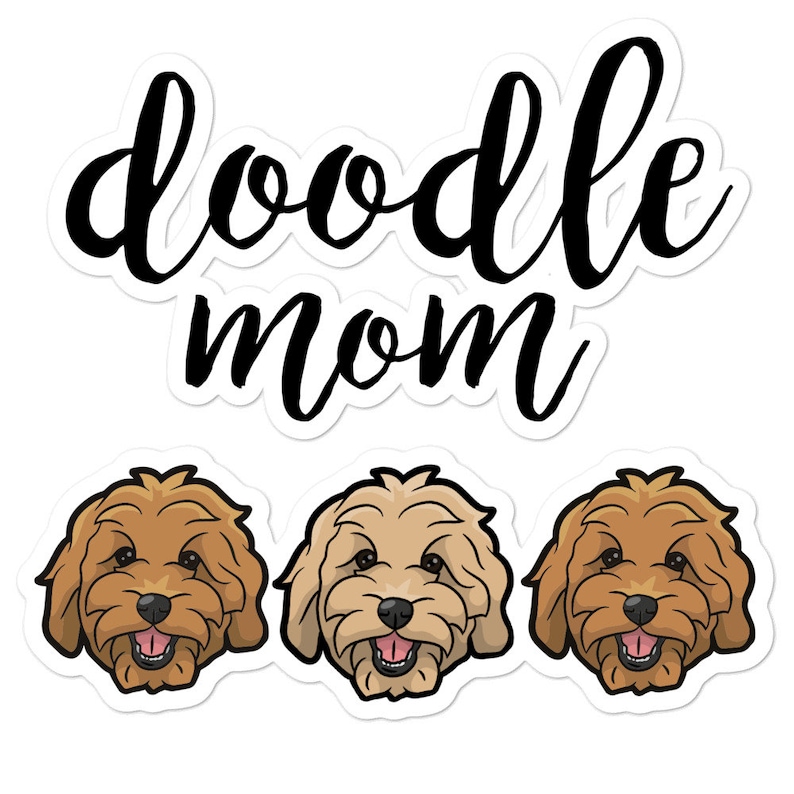 May include: Doodle Mom sticker with three doodle dog faces. The dogs have brown and cream fur, brown noses, and black eyes. The text "doodle mom" is in black cursive lettering.