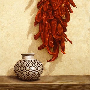 May include: A red ceramic vase with a geometric pattern sits on a wooden shelf. A bunch of dried red chili peppers hang on a beige wall behind the vase.