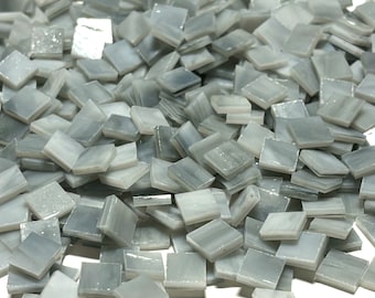 May include: A pile of small, square, gray and white glass tiles. The tiles have a marbled or striated appearance.