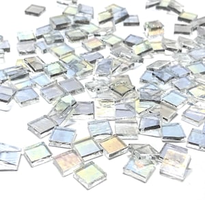 May include: A large quantity of iridescent glass mosaic tiles in a square shape. The tiles are scattered on a white surface.