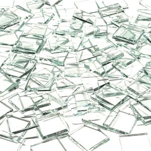 Op de afbeelding: Een grote stapel kleine, heldere glazen vierkanten. De vierkanten zijn allemaal ongeveer even groot en zijn in een willekeurig patroon gerangschikt.