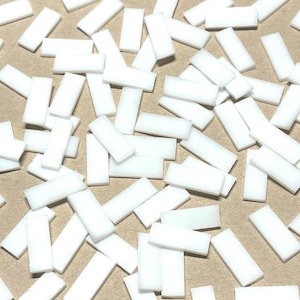 Puede incluir: Una gran cantidad de pequeñas baldosas rectangulares blancas. Las baldosas están esparcidas sobre una superficie marrón.