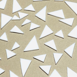 May include: A collection of white, triangular shapes scattered on a light brown surface. The triangles vary in size and are evenly distributed across the frame. The shapes have a clean, geometric appearance, creating a simple, abstract pattern.