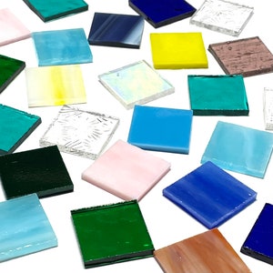May include: Assortment of small, square glass tiles in various colors, including blue, green, yellow, pink, and white. The tiles are arranged on a white surface.