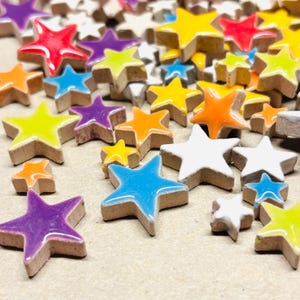May include: A collection of colorful star-shaped ceramic tiles in various sizes. The stars are glazed in vibrant colors including red, yellow, blue, orange, purple, and white. The tiles have a natural, unglazed edge.