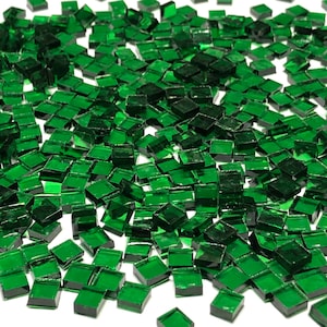 May include: A large quantity of small, square, green glass tiles. The tiles are scattered on a white surface.