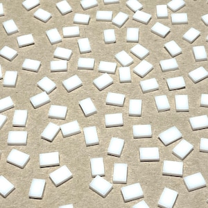 May include: A scattering of small, white, rectangular tiles. The tiles are evenly distributed across a neutral-toned surface. Each tile has a slightly raised, three-dimensional appearance, suggesting a textured surface. The overall effect is clean and minimalist.