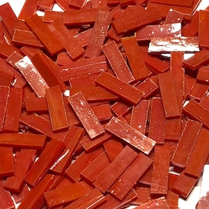 Könnte beinhalten: Ein Haufen kleiner, rechteckiger, orangefarbener Glasfliesen. Die Fliesen haben eine schimmernde, irisierende Oberfläche.