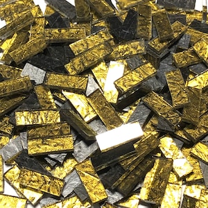 Puede incluir: Un montón de pequeñas baldosas de vidrio rectangulares en negro y dorado. Las baldosas doradas tienen un acabado metálico.