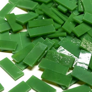 May include: A collection of small, rectangular glass tiles in a solid, opaque grass green color. Each tile features a smooth, flat surface with straight edges, arranged in a scattered pile, showcasing a consistent shade and uniform shape.