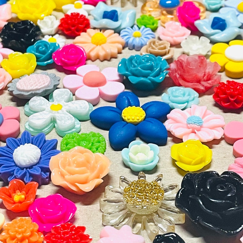 May include: Assortment of colorful resin flower embellishments in various shapes and sizes. The flowers are made of a shiny, smooth resin and have a variety of colors, including pink, blue, green, yellow, and red.