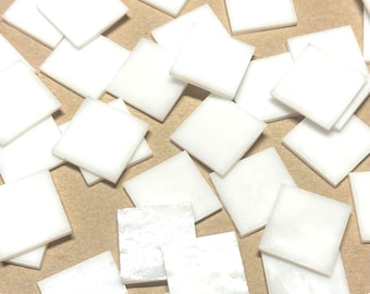 Puede incluir: Una colección de azulejos cuadrados blancos, algunos con un acabado nacarado, esparcidos sobre una superficie marrón.