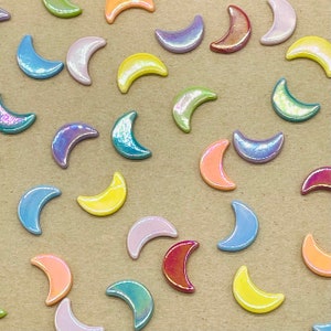 May include: Assortment of colourful crescent moon shaped ceramic tiles. The tiles are in various shades of blue, green, yellow, pink, and purple.