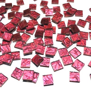 May include: A scattering of small, square, iridescent glass tiles in a deep pink color. The tiles have a metallic sheen and a textured surface.