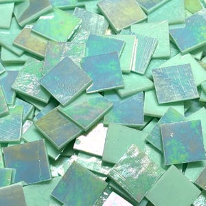 May include: A collection of square mosaic tiles in shades of green, blue, and iridescent white. The tiles have a glossy finish and vary in colour and texture. Suitable for craft projects.