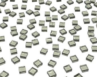May include: A scattering of small, square, light gray glass tiles on a white background.