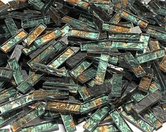 May include: A pile of green and gold iridescent glass mosaic tiles. The tiles are rectangular and have a metallic finish.