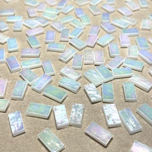 May include: A collection of iridescent white rectangular tiles, scattered on a brown surface. The tiles have a subtle shimmer and are perfect for crafting or home decor projects.