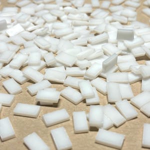 May include: A large quantity of small, white, rectangular adhesive squares. The squares are scattered on a brown surface.