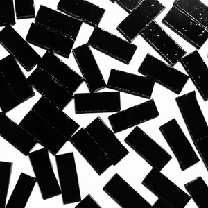 May include: A collection of black rectangular tiles scattered on a white surface. The tiles are glossy and have a slightly textured surface.