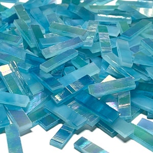 May include: A pile of light blue iridescent glass tiles in a rectangular shape. The tiles are scattered on a white surface.