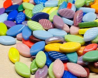 May include: A pile of multi-coloured, oval glass beads. The beads are in shades of red, blue, green, yellow, and purple. Some have textured surfaces, others are smooth. The beads are scattered, creating a vibrant and playful display.