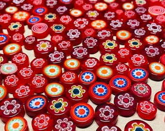 Puede incluir: Una colección de azulejos de vidrio rojo con diseños florales blancos y amarillos. Los azulejos están dispuestos en un patrón aleatorio.